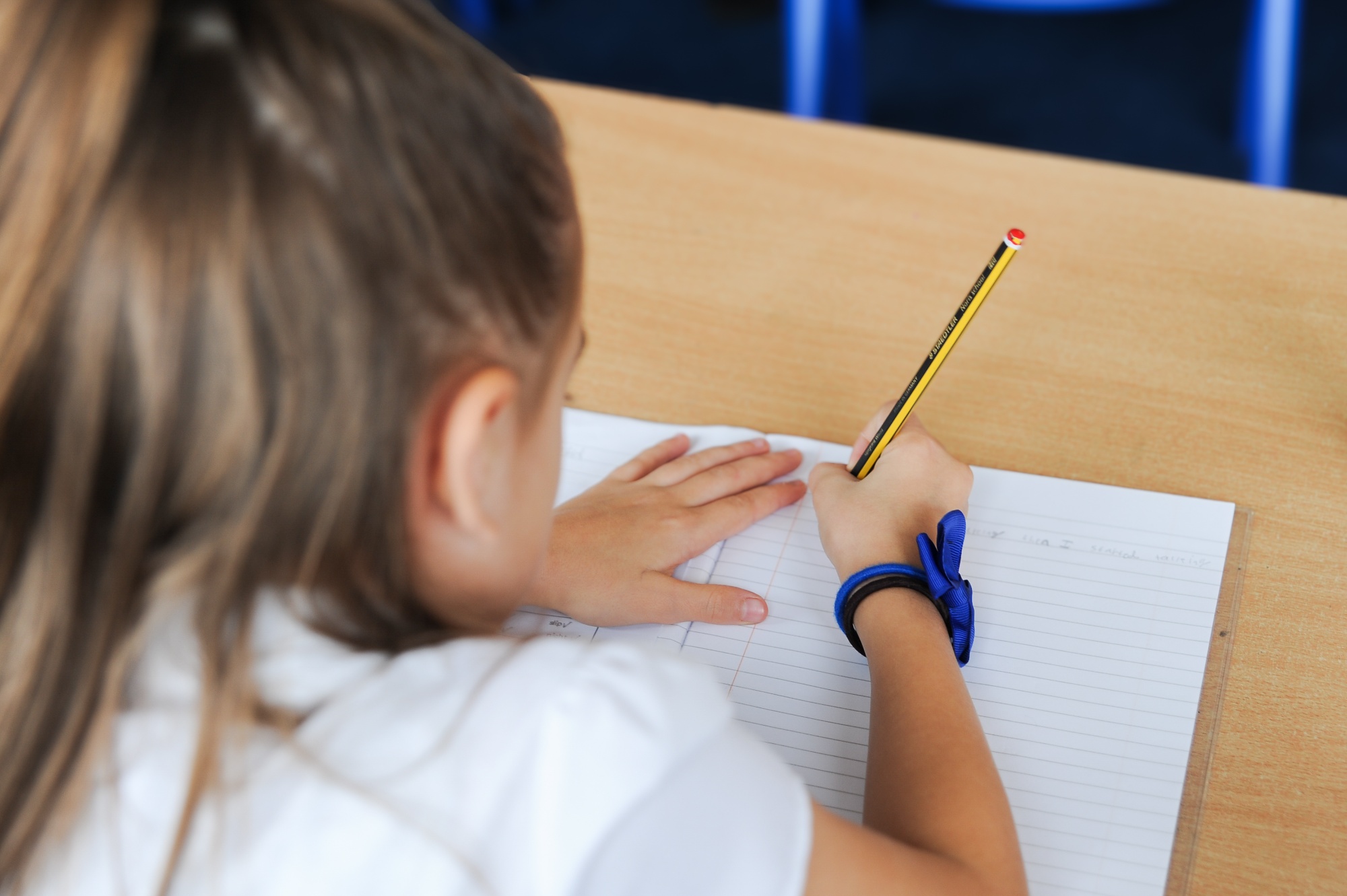 female child writing with a pencil in an lined book 